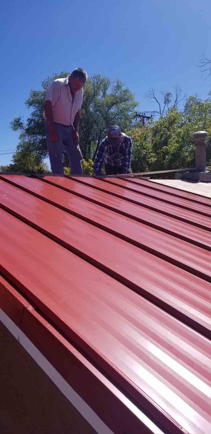 Two men are working on a red metal roof.