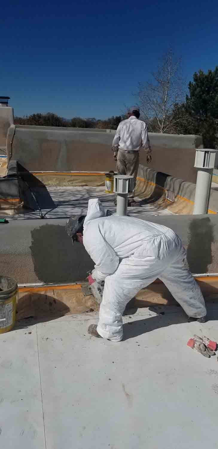 A man in a white suit is painting a roof.