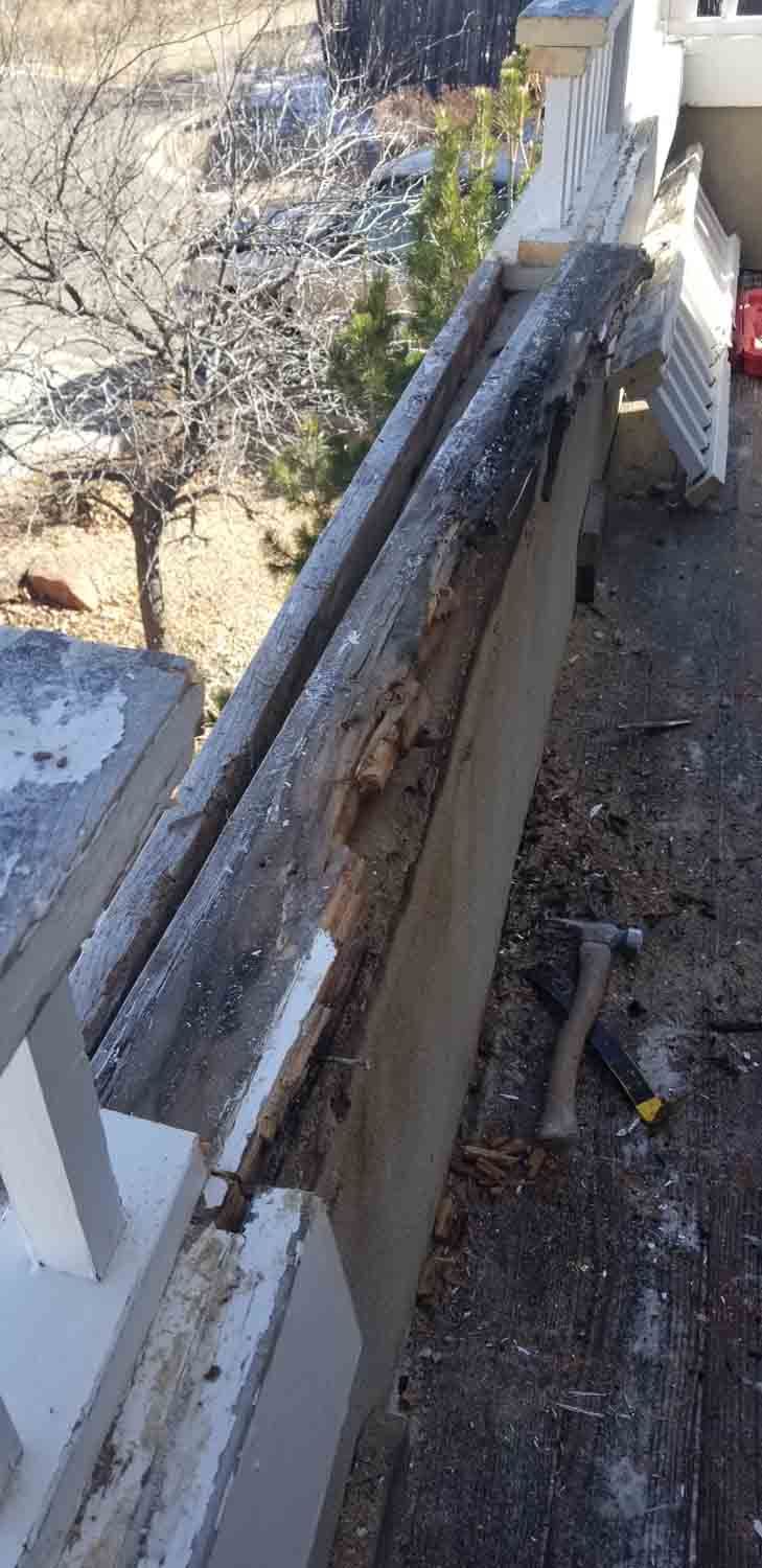 A hammer is sitting on the ground next to a wooden railing.