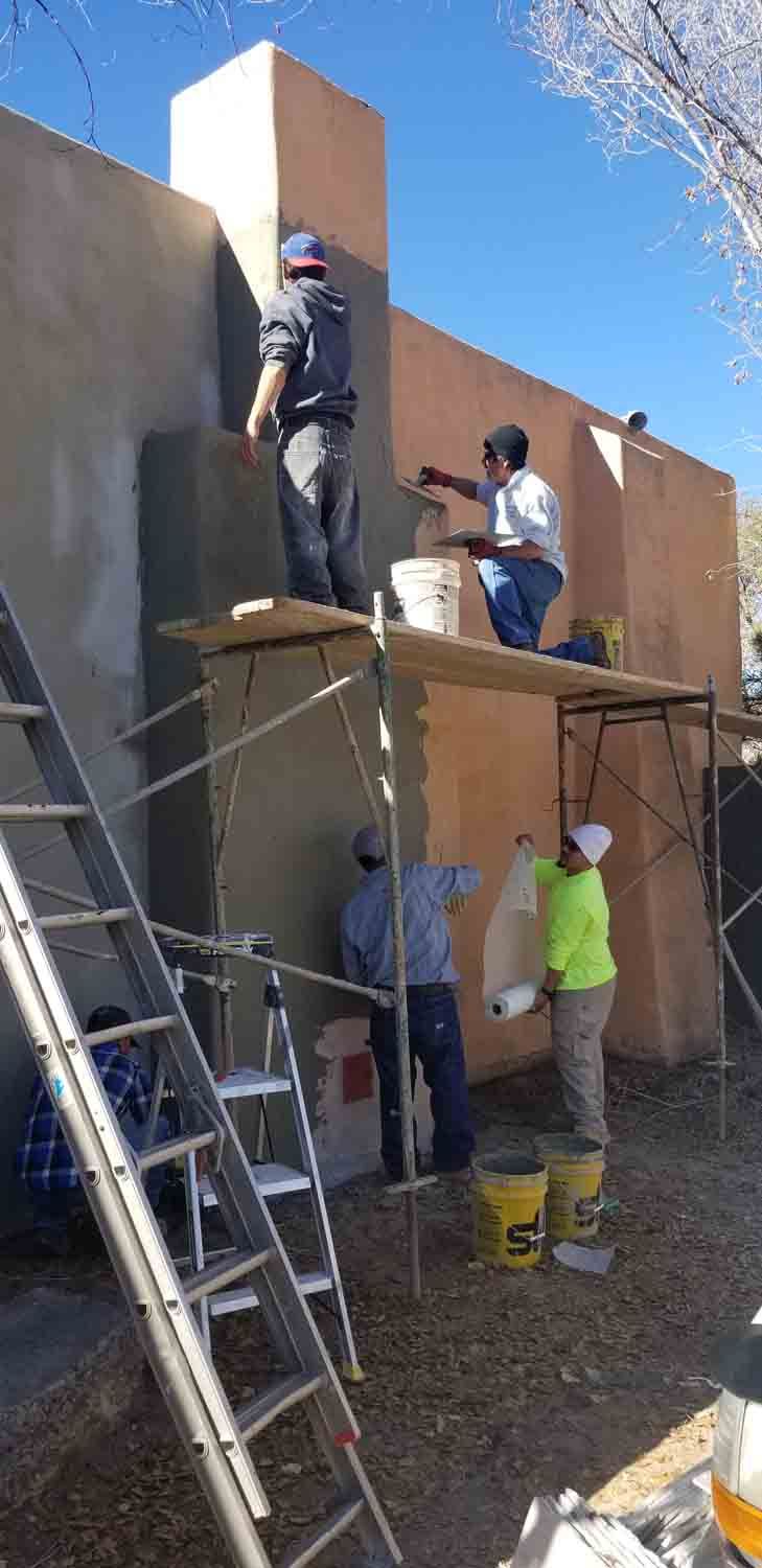 A group of people are painting a wall on a scaffolding.