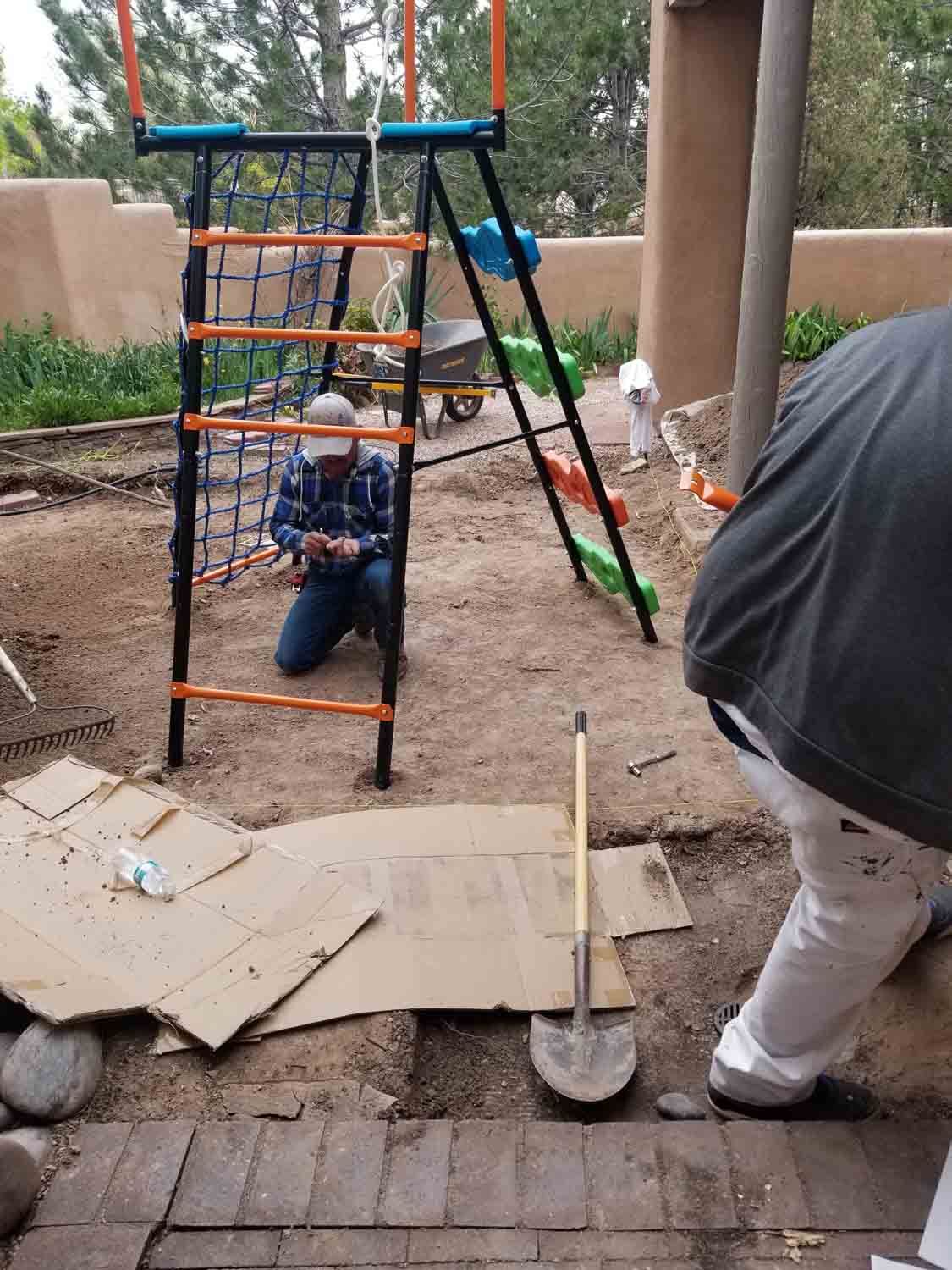 A man is kneeling in the dirt in front of a playground.