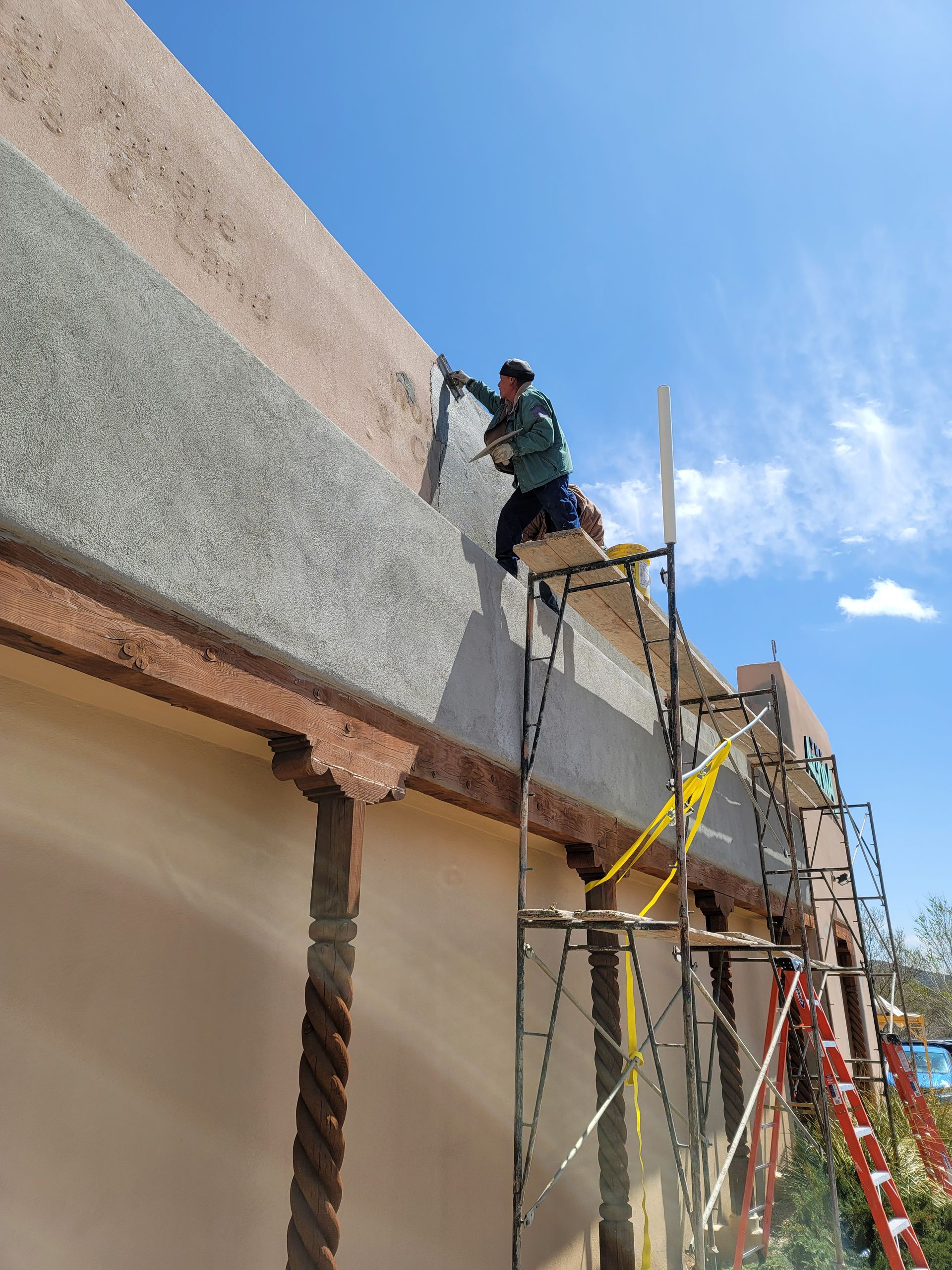 A man is painting the side of a building on a scaffolding.