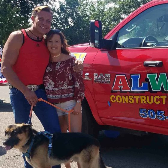 A man and woman standing next to a red truck that says alm construct 505