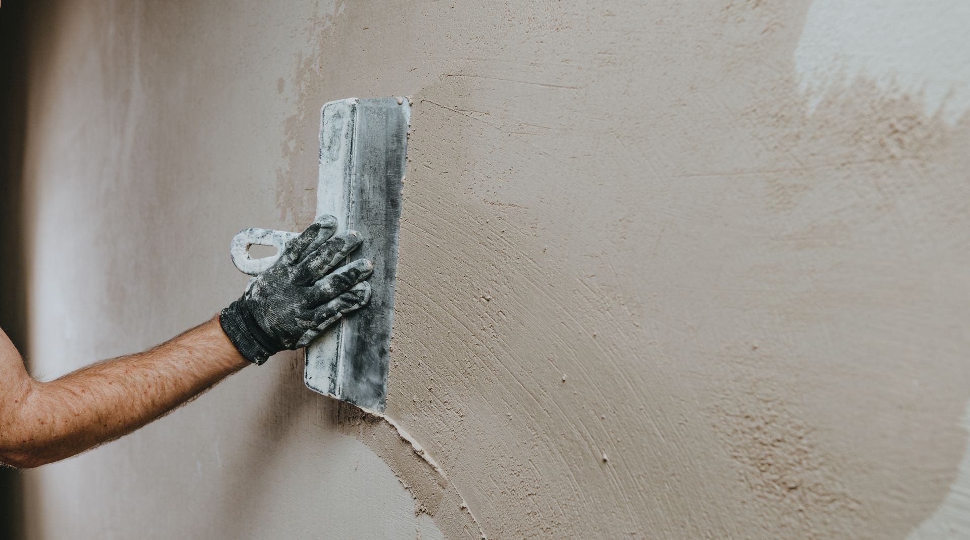 Gloved hand using a trowel to apply plaster to a wall.