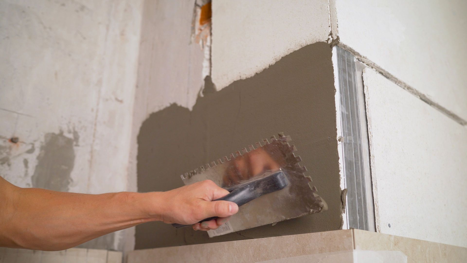 Person applying gray plaster to a wall corner with a trowel during renovation.