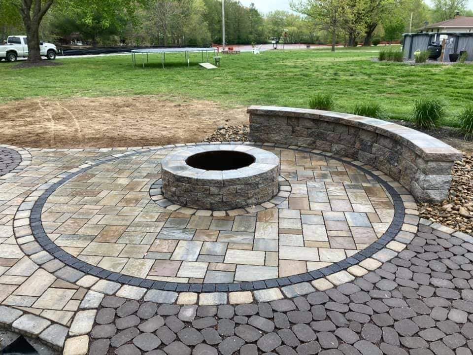 Circular stone patio with fire pit, curved retaining wall, and varying brick patterns in yard.