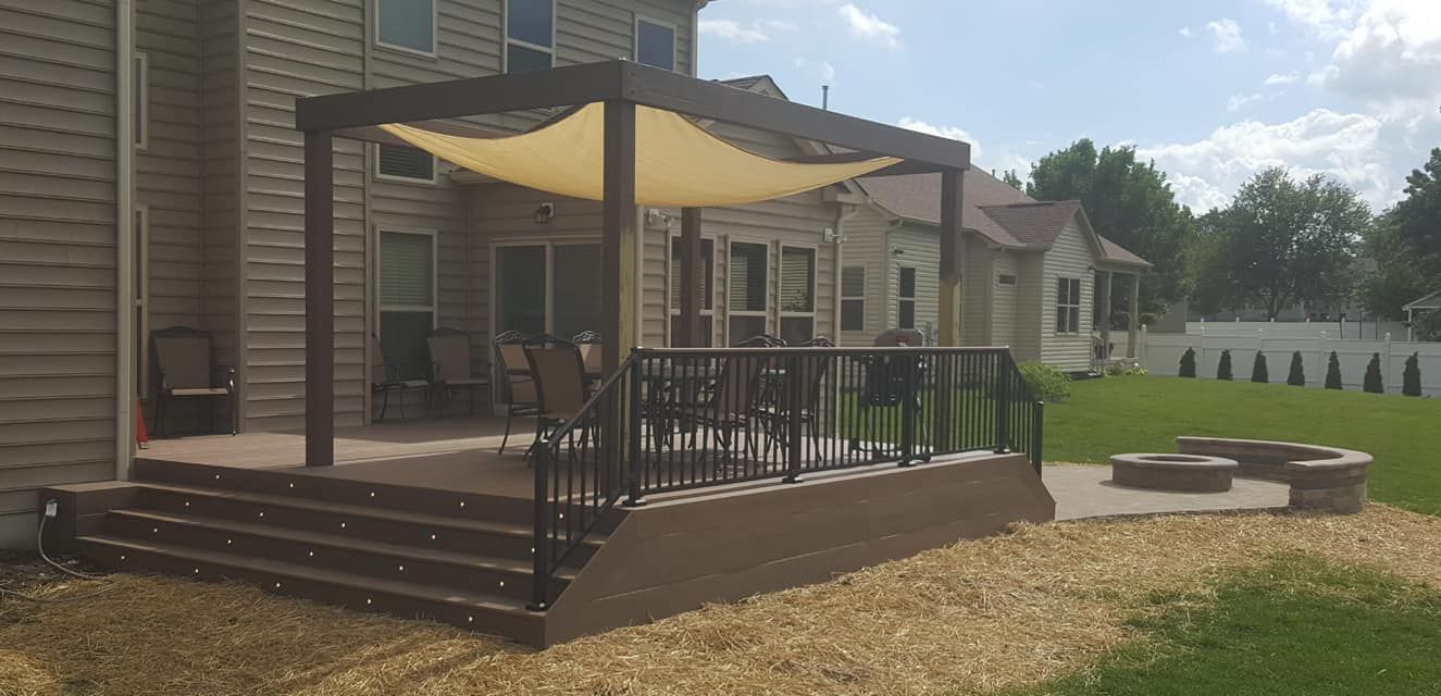 Backyard deck with pergola and shade sail, overlooking a yard with fire pit.