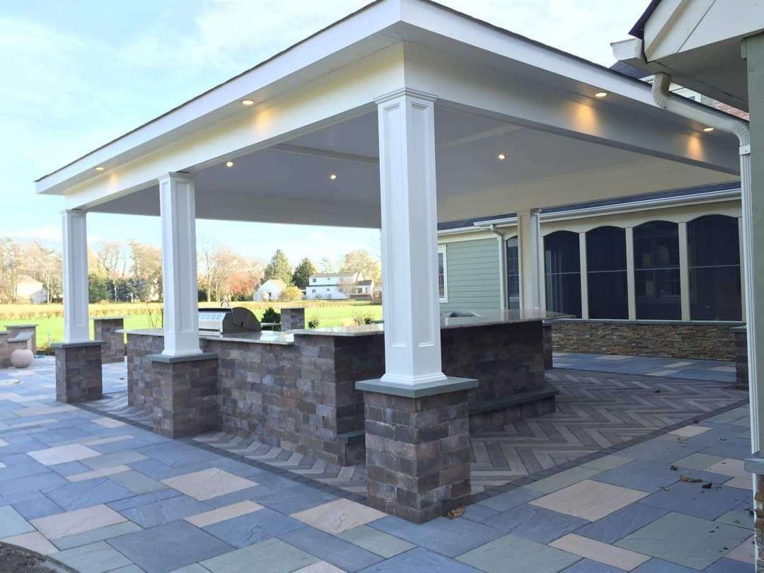 Outdoor kitchen with brick facing, columns, and a covered roof on a paved patio.