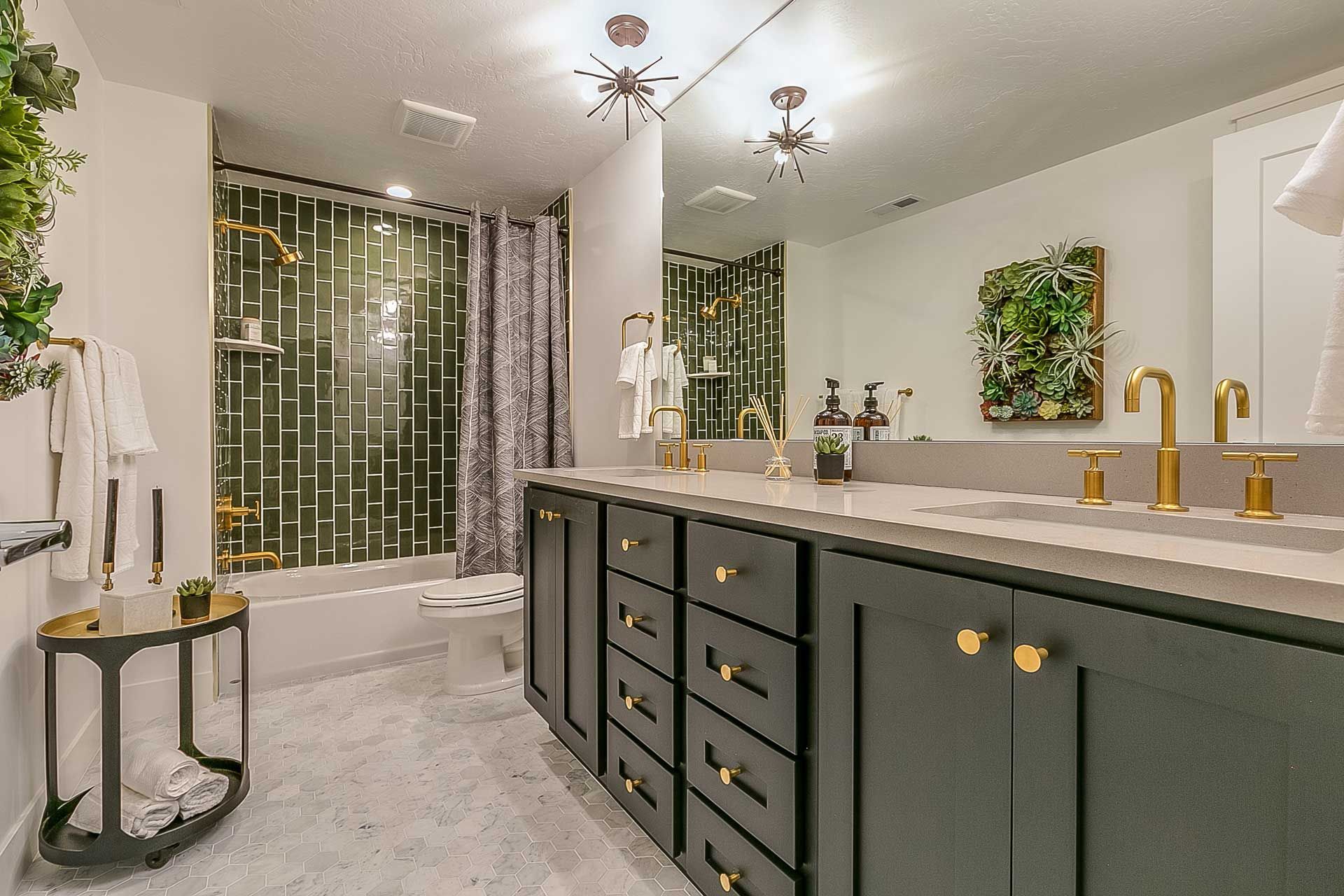 Modern bathroom with a dark gray vanity, gold fixtures, and a glass-tiled shower area.