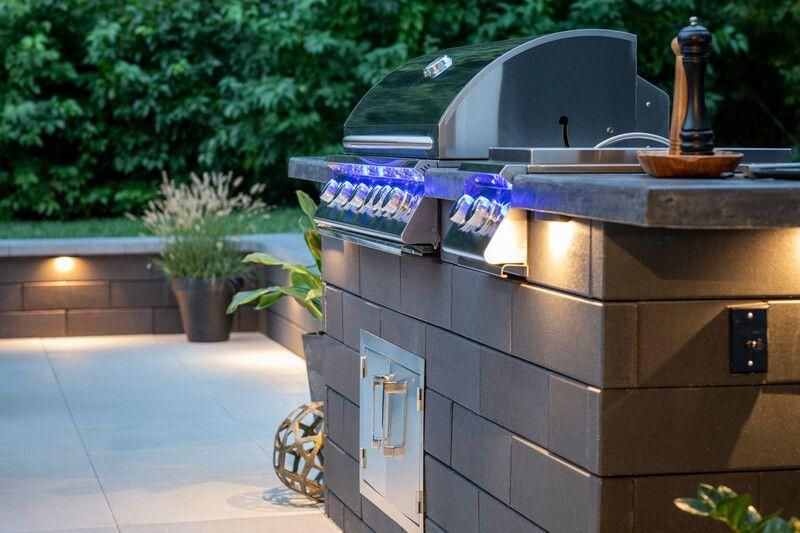 Outdoor kitchen with built-in grill, brick facade, and ambient lighting on patio.