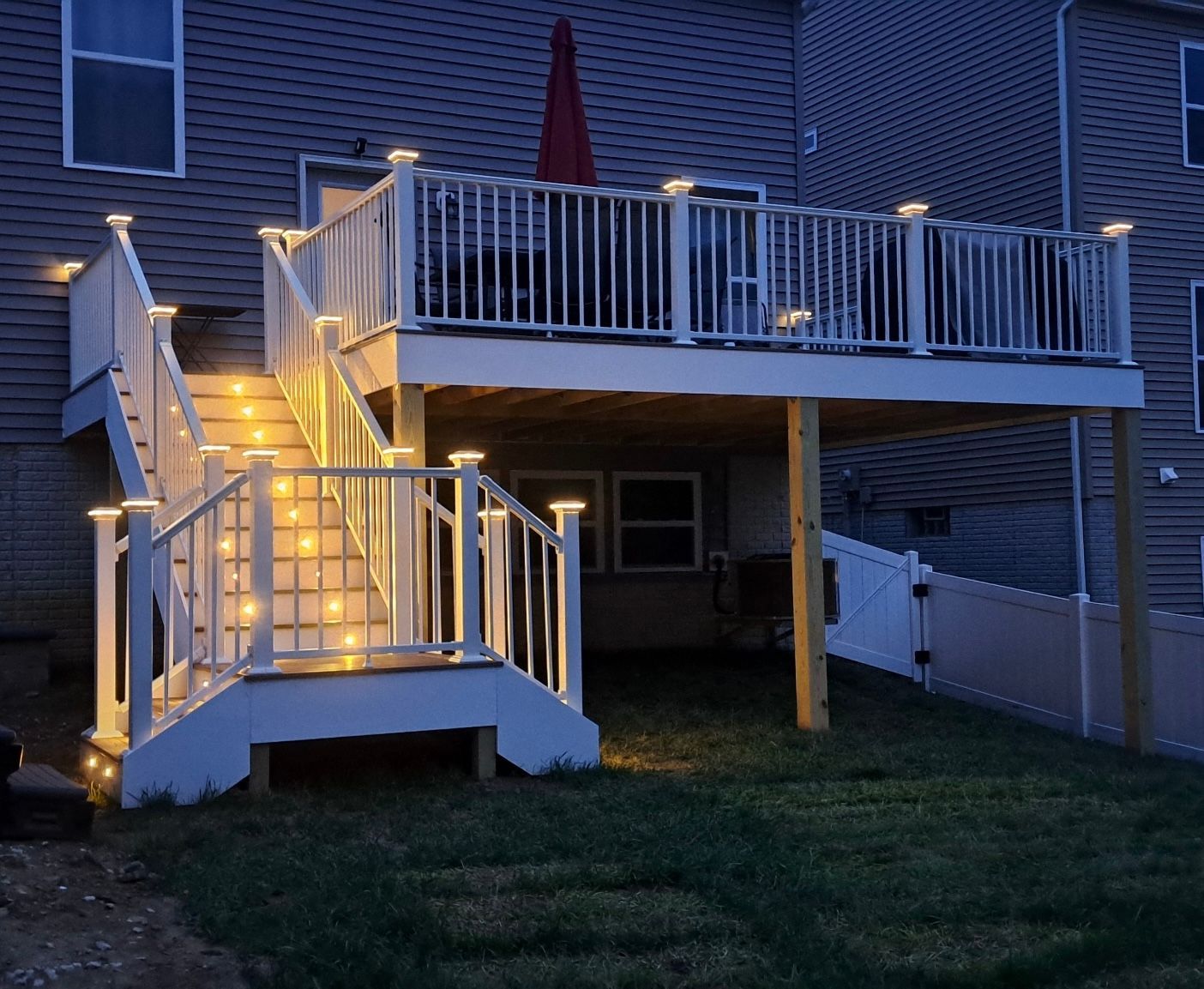 Lit deck at night with stairs, railing lights, and a red umbrella on the upper level.