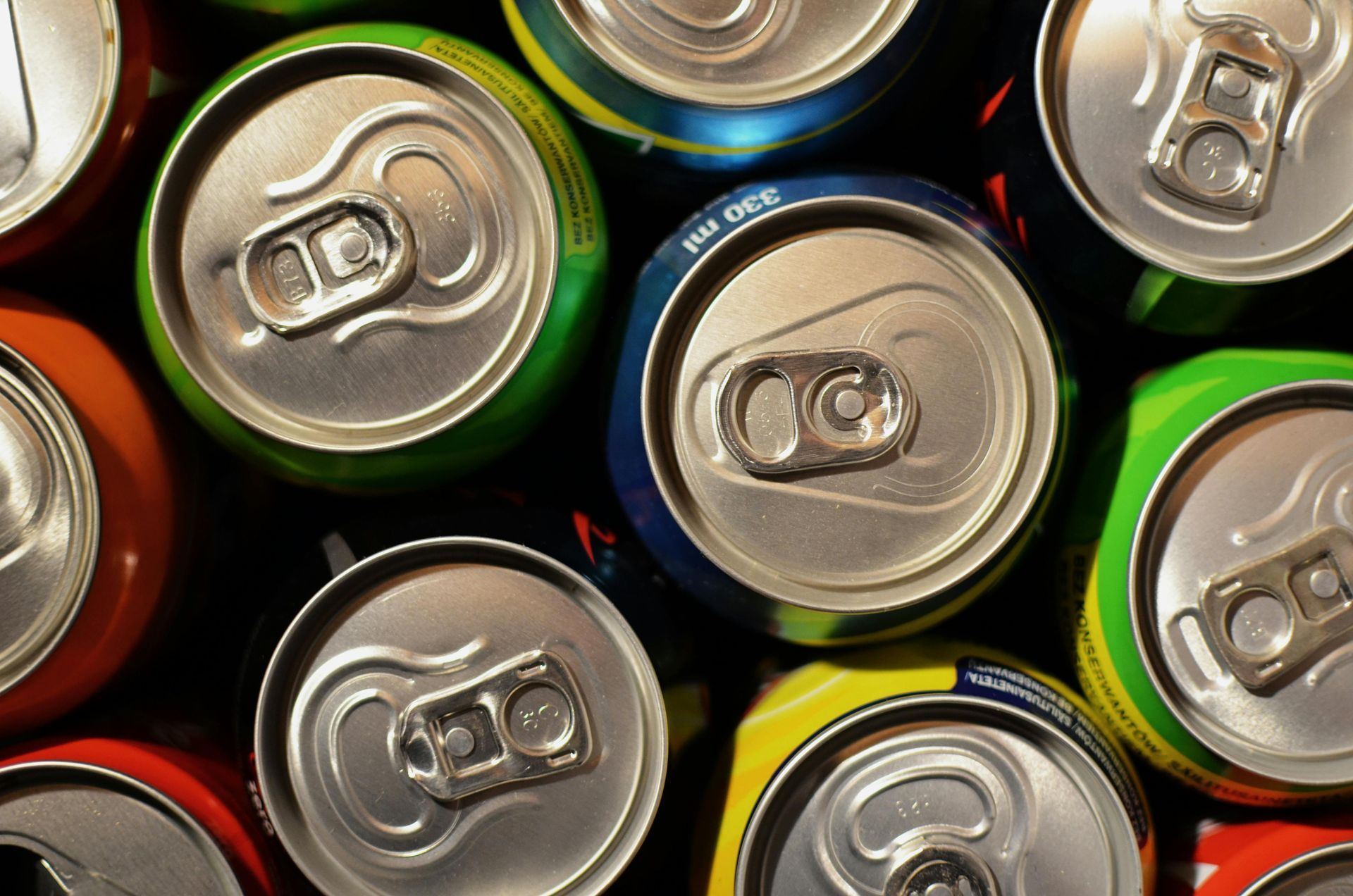 Close-up of colorful soda cans from above. Various colors and some with pull tabs visible.
