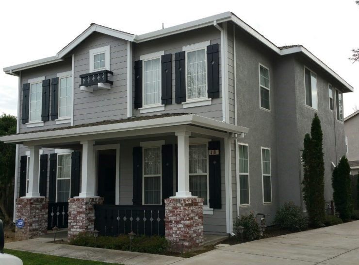 A grey house with black shutters on the windows
