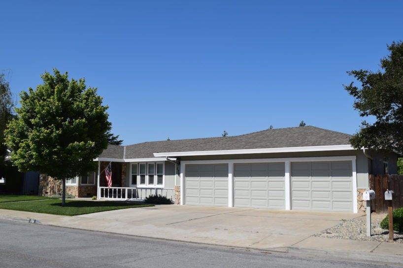 A house with three garage doors and a tree in front of it
