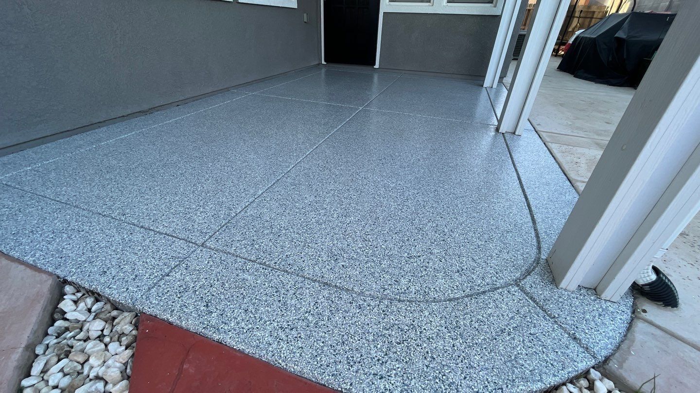 A porch with a gray concrete floor and a red brick walkway.