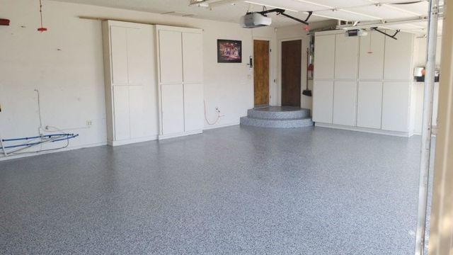 An empty garage with a gray floor and white cabinets.