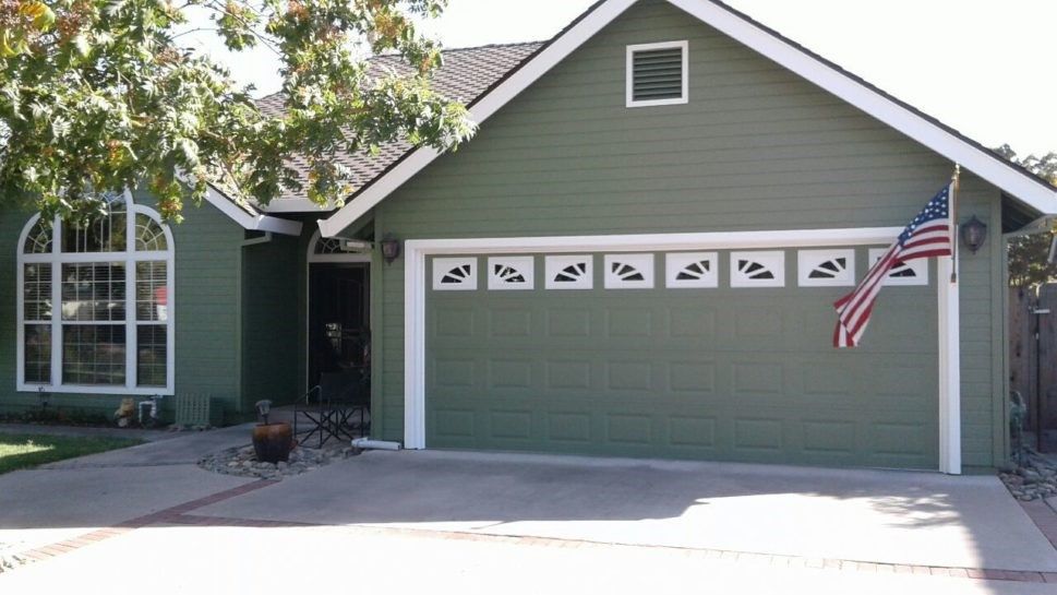 A green house with a large garage door and an american flag