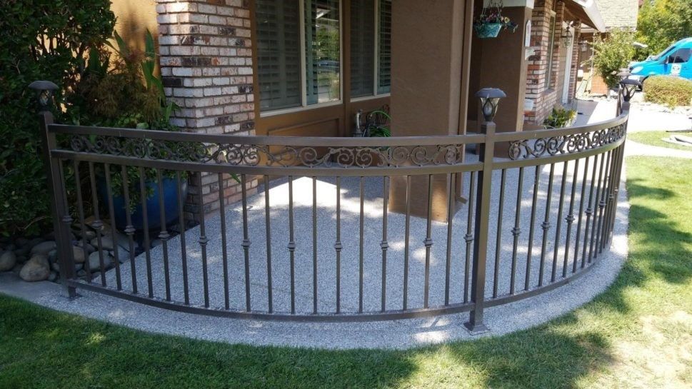 A wrought iron fence is surrounding a patio in front of a house.