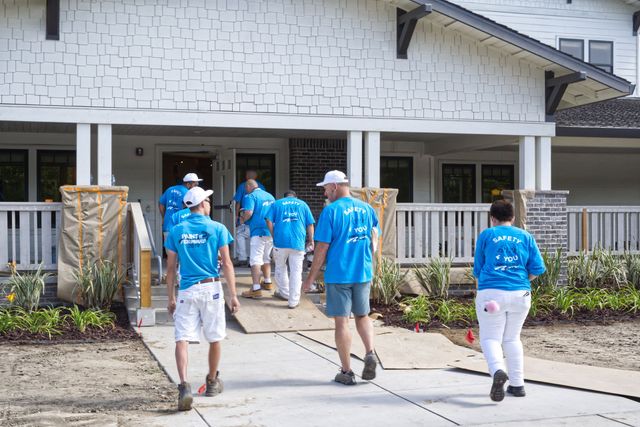 A group of people in blue shirts are walking in front of a house.