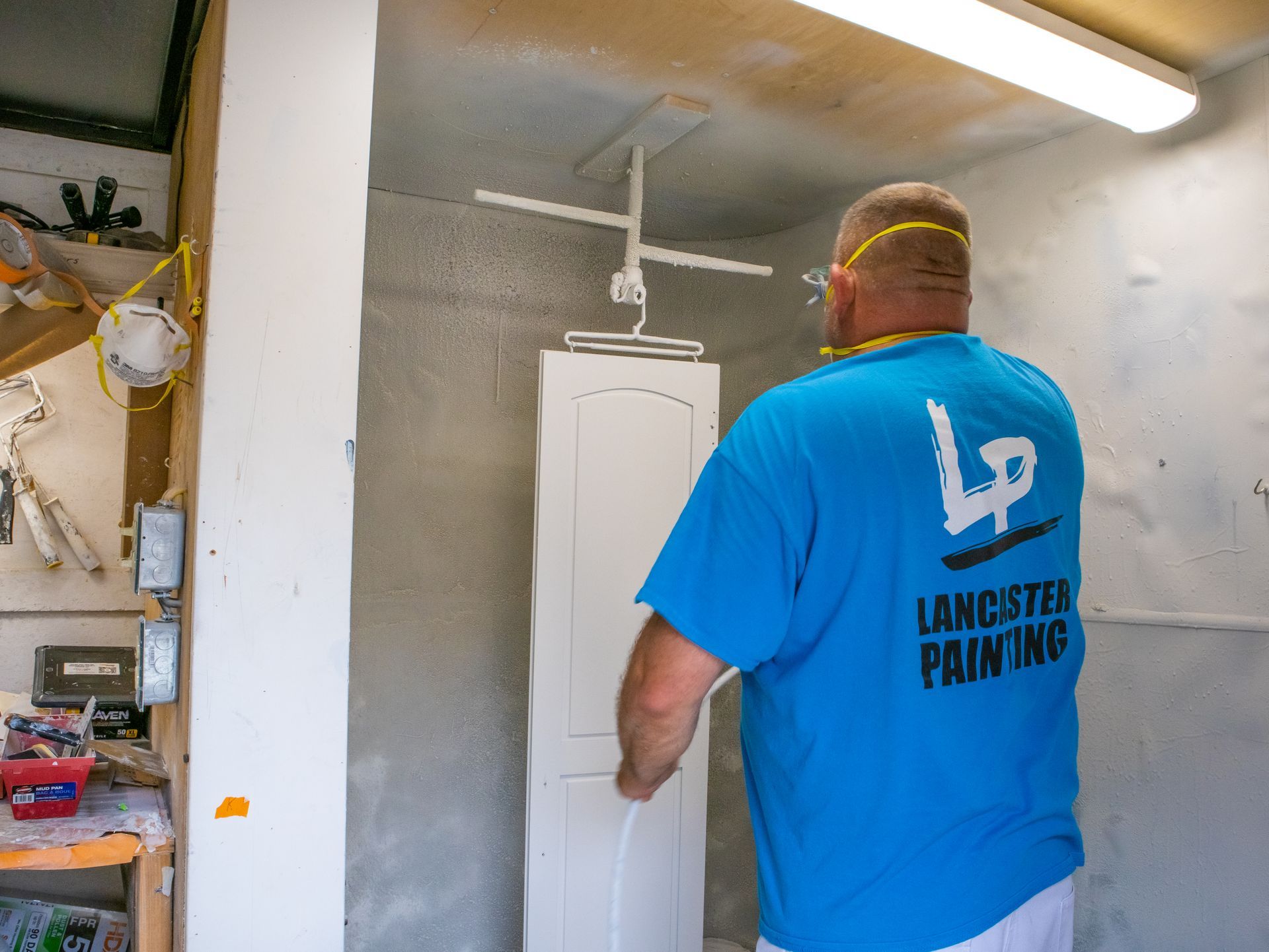 A man wearing a blue shirt that says lancaster painting is painting a door.