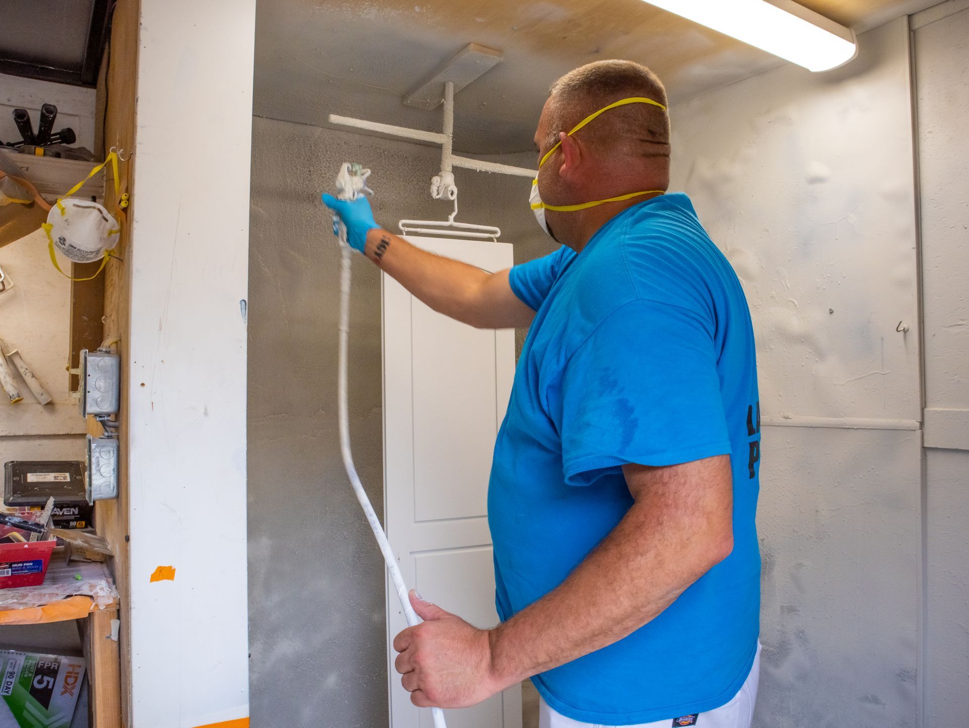 A man in a blue shirt is spray painting a white door.