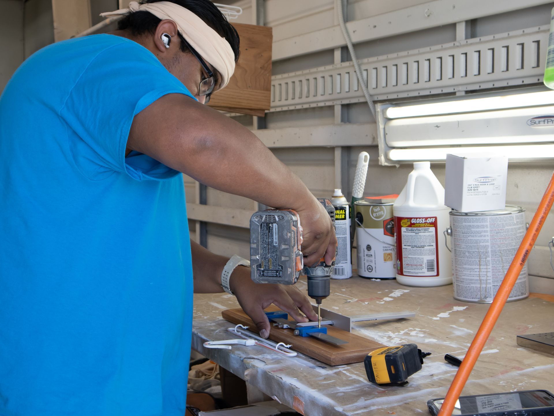 A man in a blue shirt is using a drill on a piece of wood.