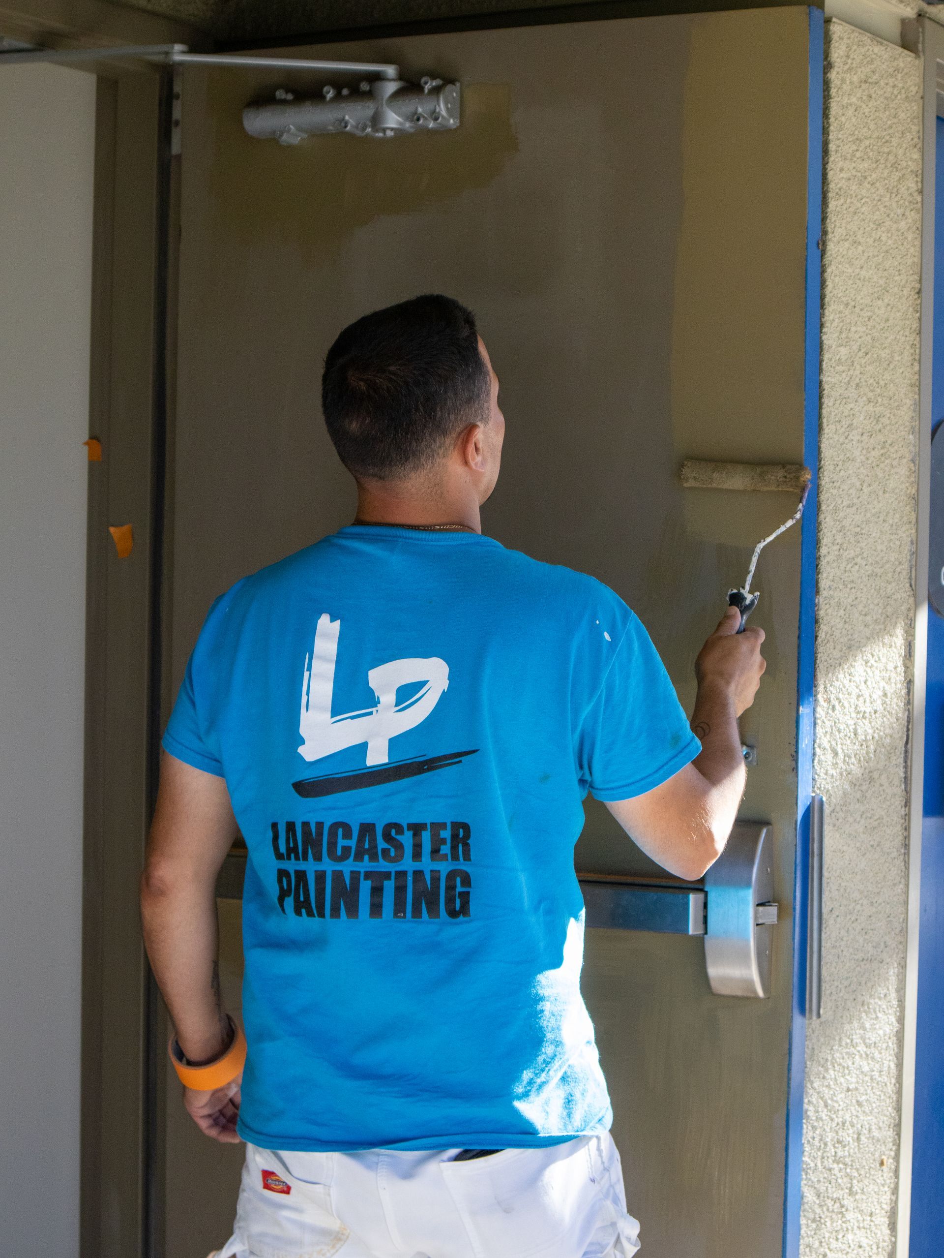 A man wearing a blue lancaster painting shirt paints a door
