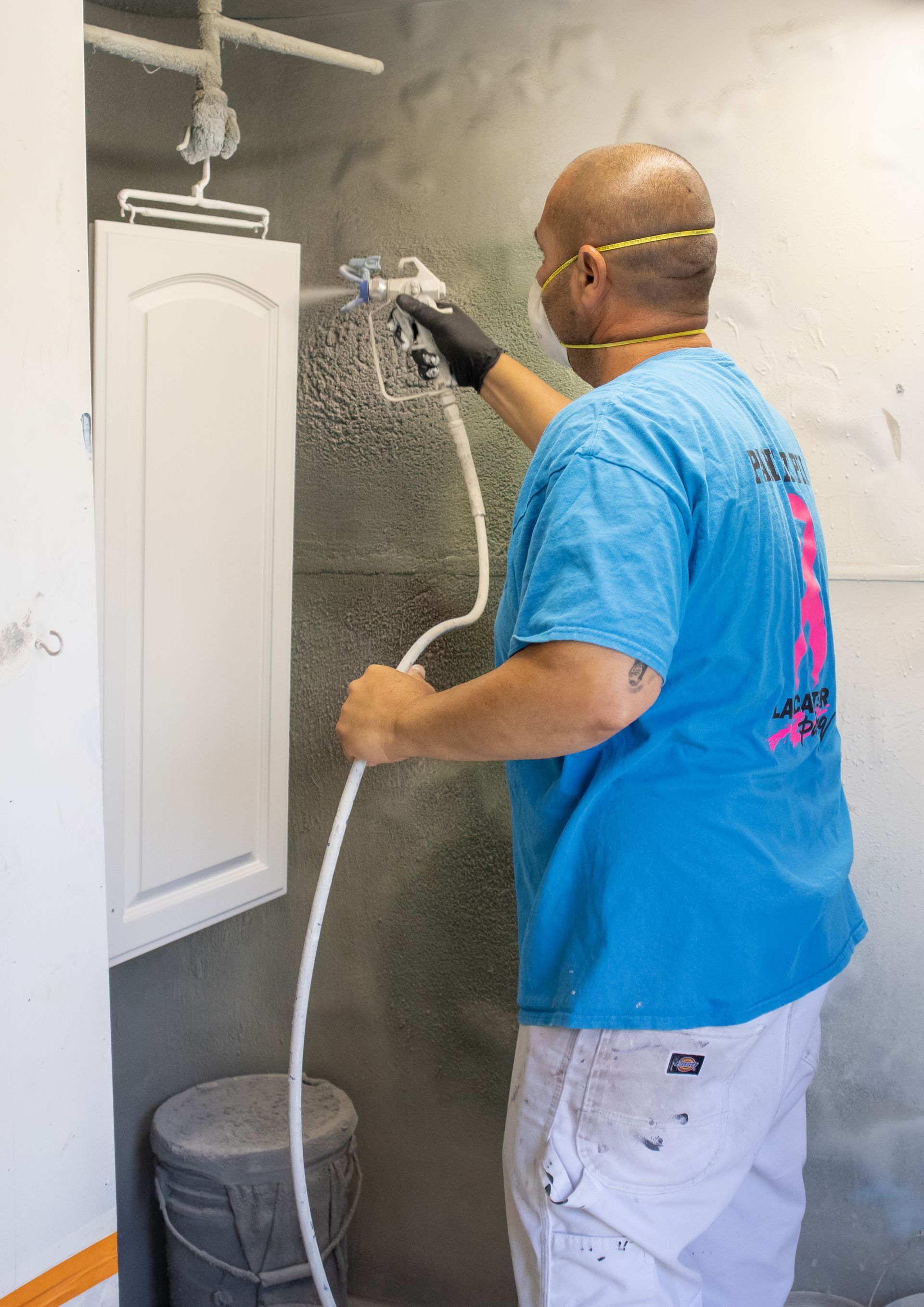 A man in a blue shirt is spray painting a cabinet door.