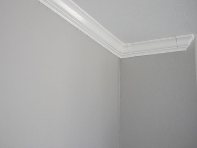 A corner of a room with white walls and a white cornice.