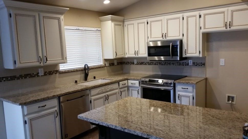A kitchen with white cabinets , granite counter tops , stainless steel appliances and a large island.
