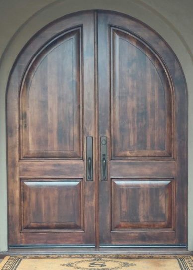 A pair of arched wooden doors with a rug in front of them