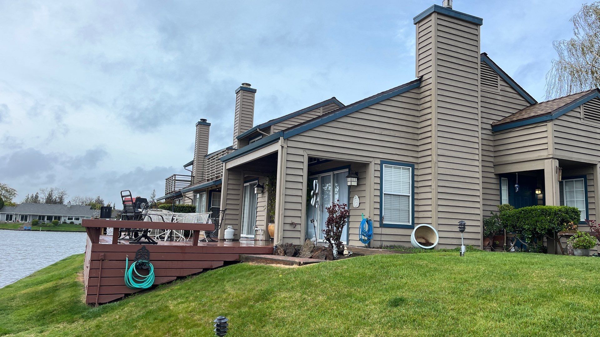 A large house is sitting on top of a lush green hill next to a lake.