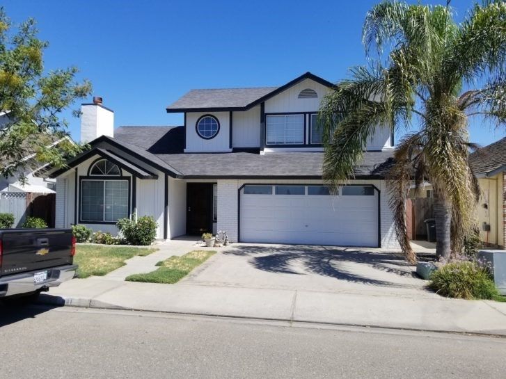 A black truck is parked in front of a white house