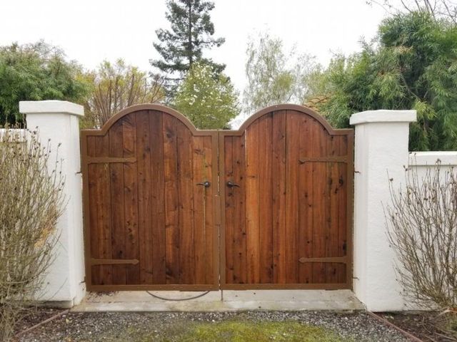 A wooden gate is surrounded by white pillars and bushes.
