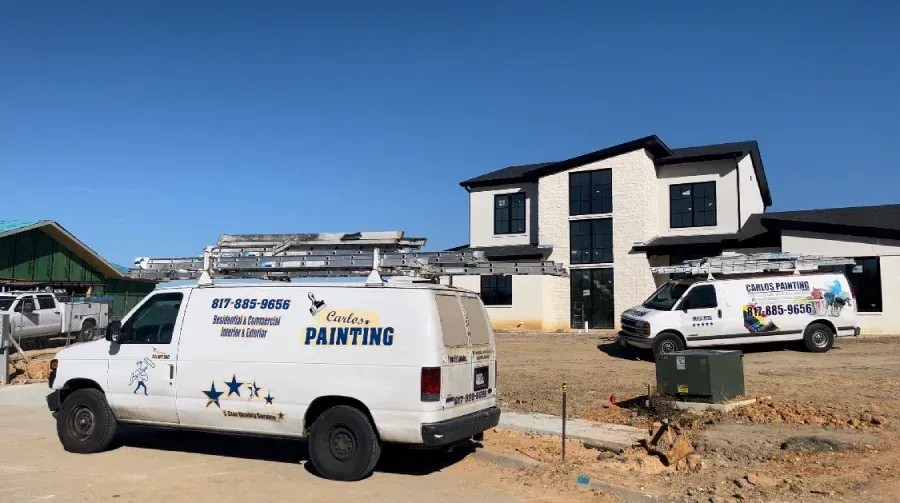 Two painting vans are parked in front of a house under construction.