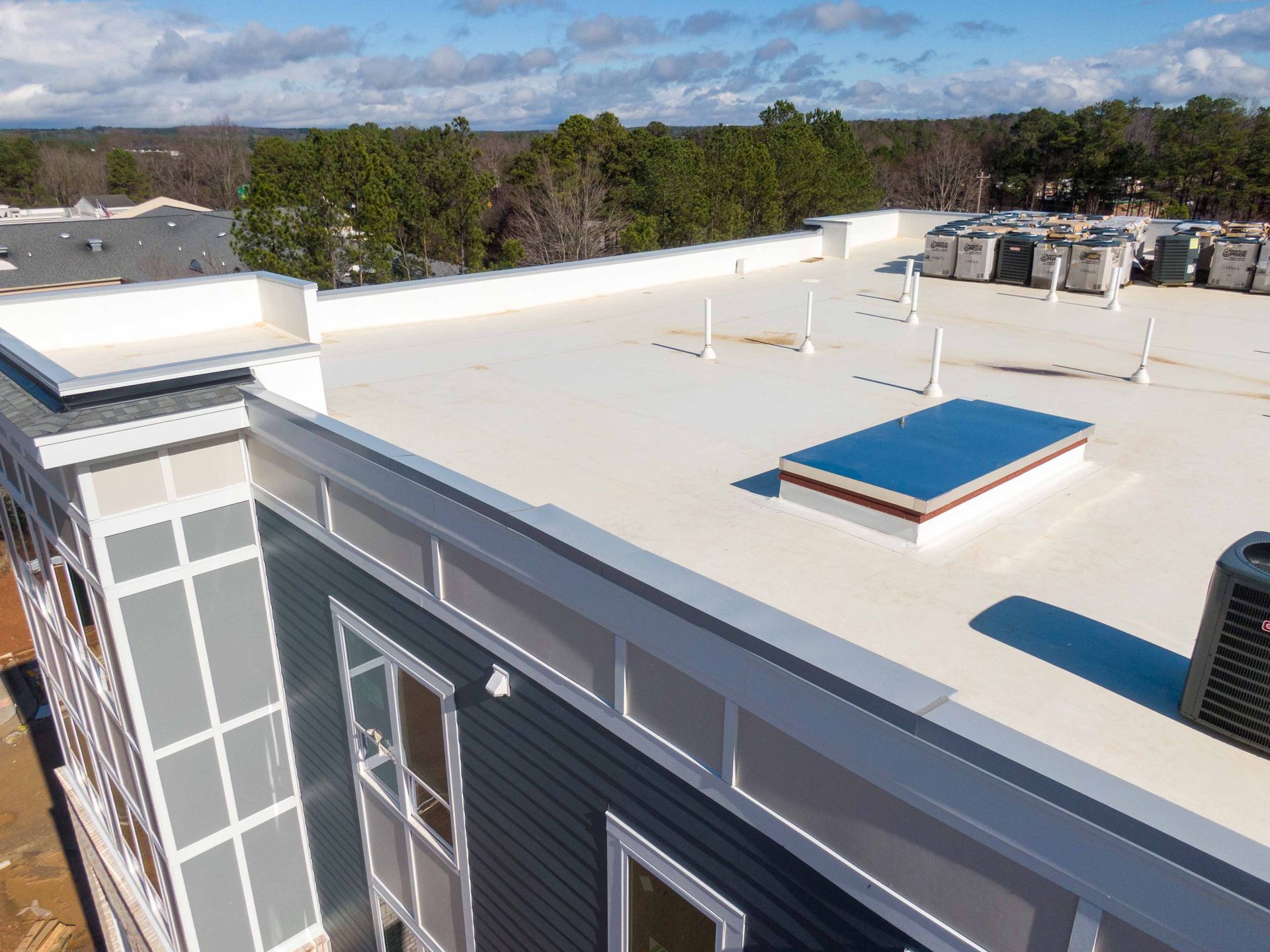 Aerial view of a building with a white flat roof, air conditioning units, and blue sky.