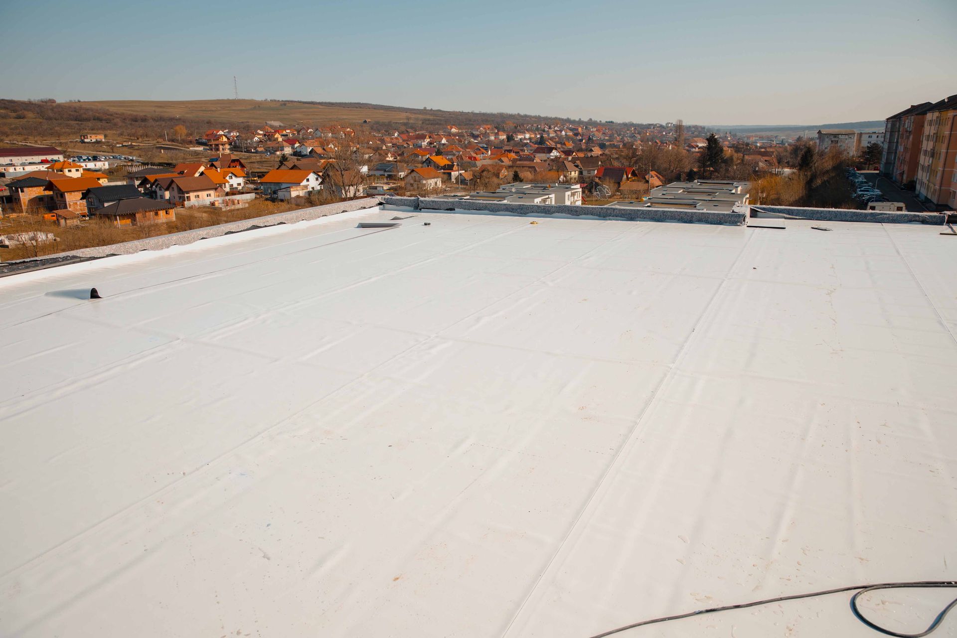 White flat roof of a building with a cityscape in the background on a sunny day.