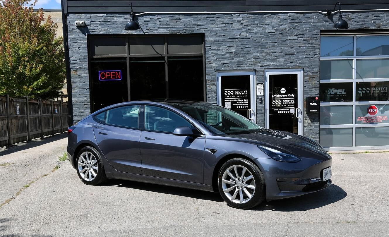 Dark gray sedan parked outside a black storefront on a sunny day