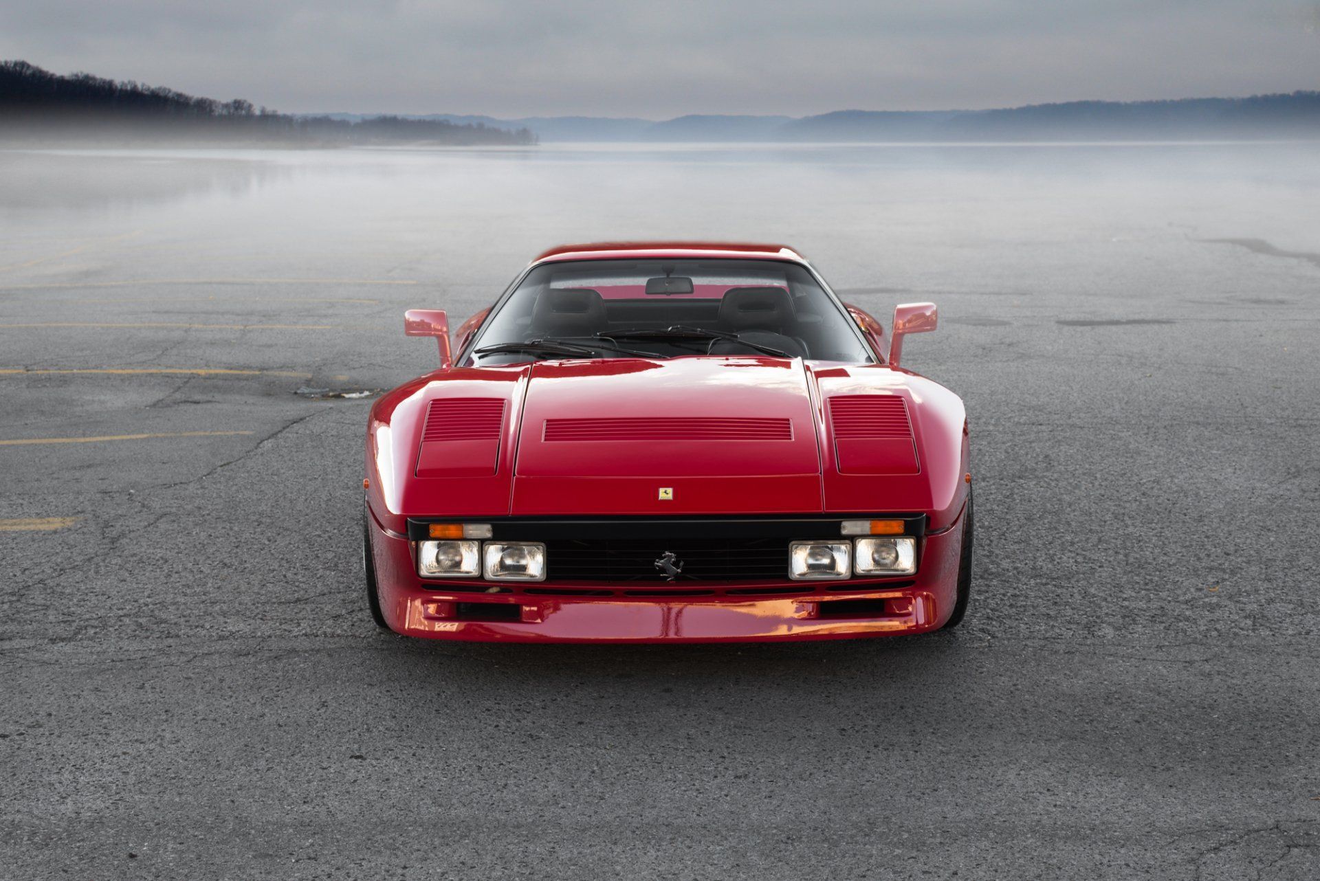 Red sports car parked on wet pavement under a misty sky, front view.