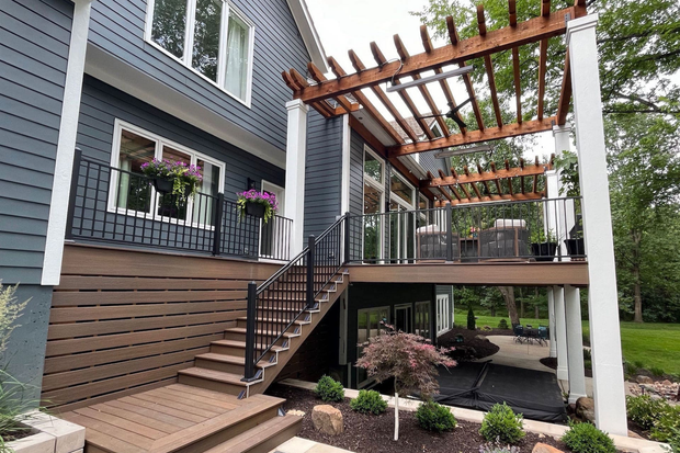 Deck with pergola attached to a blue house, featuring stairs, railings, and outdoor seating.