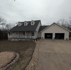 Beige house with a porch, attached garage, and concrete driveway on a cloudy day.