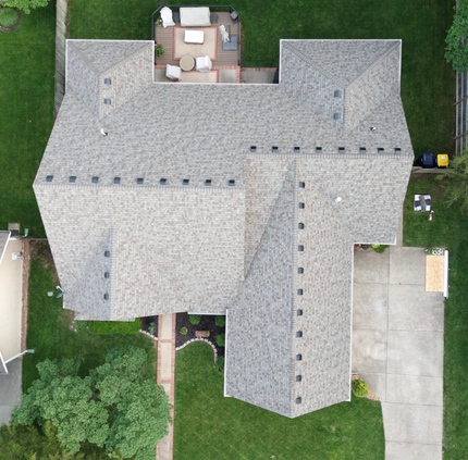 Overhead view of a gray roofed house with a patio, concrete driveway, and green yard.