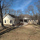 Ranch-style house with tan and brown exterior, long walkway, and bare trees against a blue sky.
