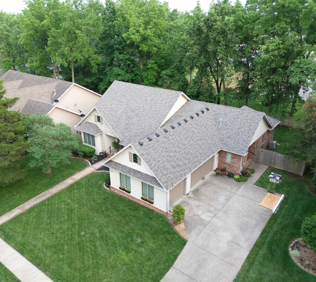 An aerial view of a house with a gray roof surrounded by trees.