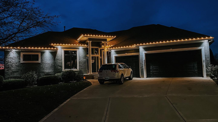 A car is parked in front of a house that is lit up at night.