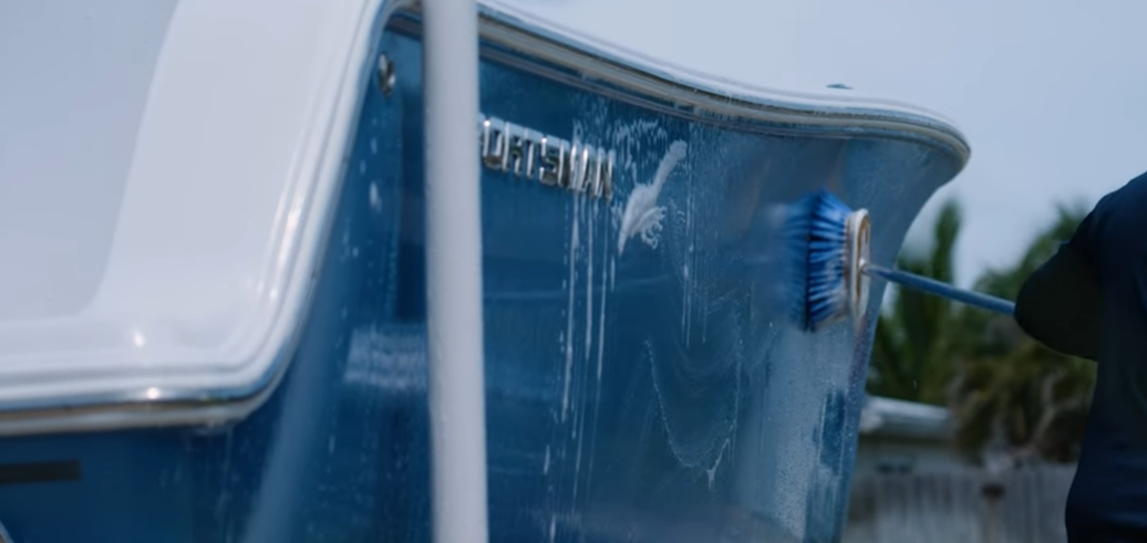 worker with broom and soap washing side of the boat
