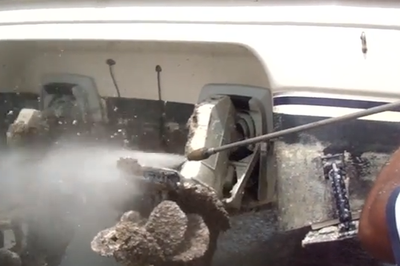 worker with power hose cleaning and removing marine fouling out of the motor of the boat