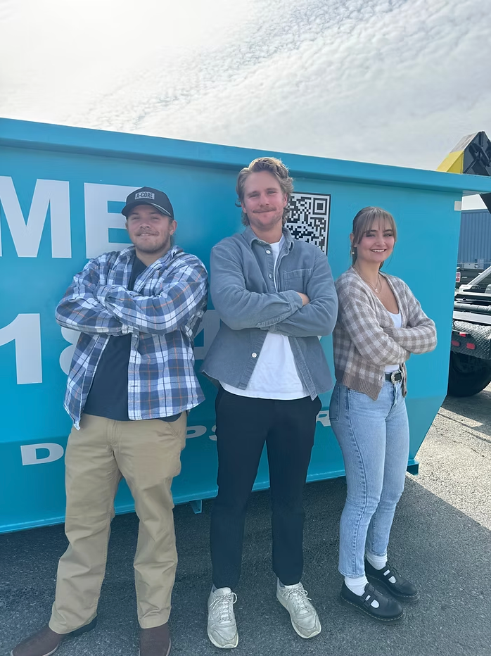 bailey stewart and team with arms crossed stand in front of a blue dumpster.