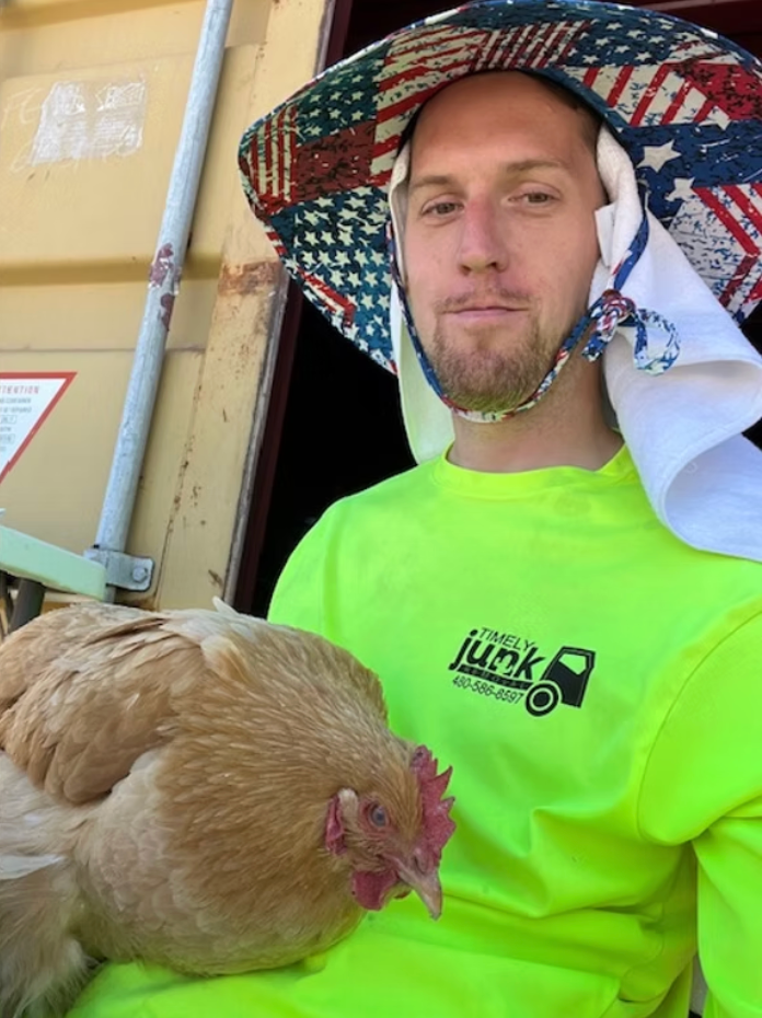 Darrell Waller in patriotic hat and neon shirt holding a chicken outdoors.