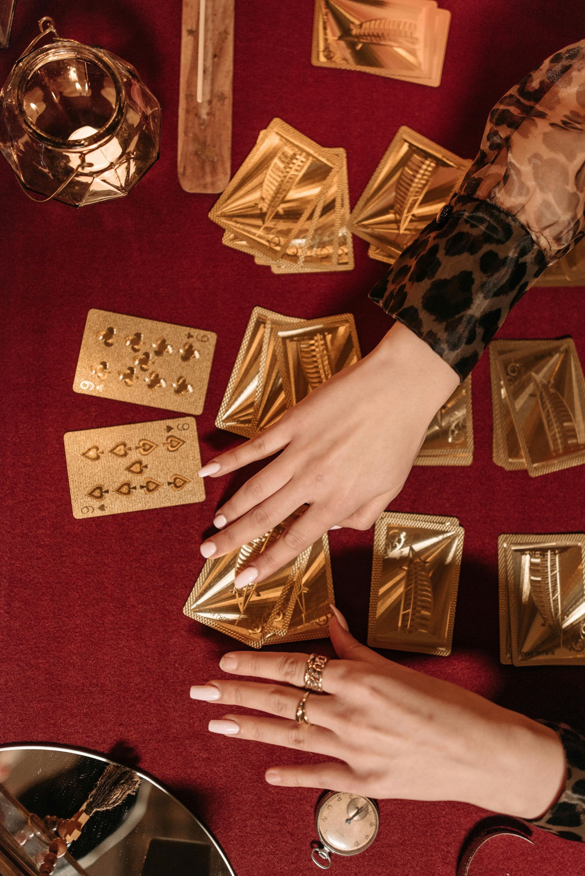 Hands with rings selecting gold tarot cards on a red cloth.